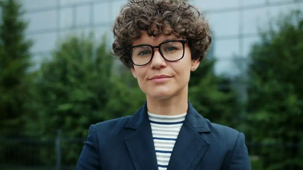 A woman with short curly hair wearing glasses and a blue suit.