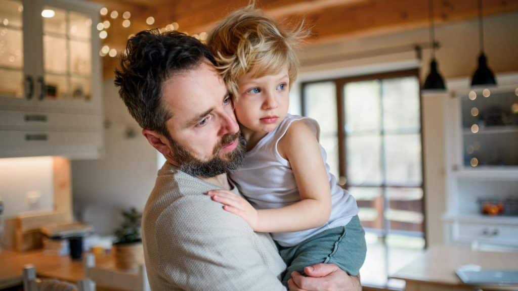 A father holding his young child in a kitchen.