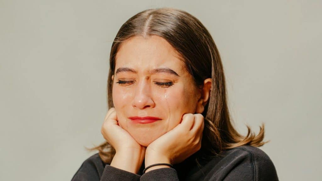 Close-up of a woman with long hair crying, resting her chin on both hands.