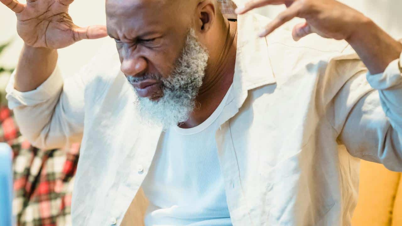 A man grimacing with his hands raised in frustration.