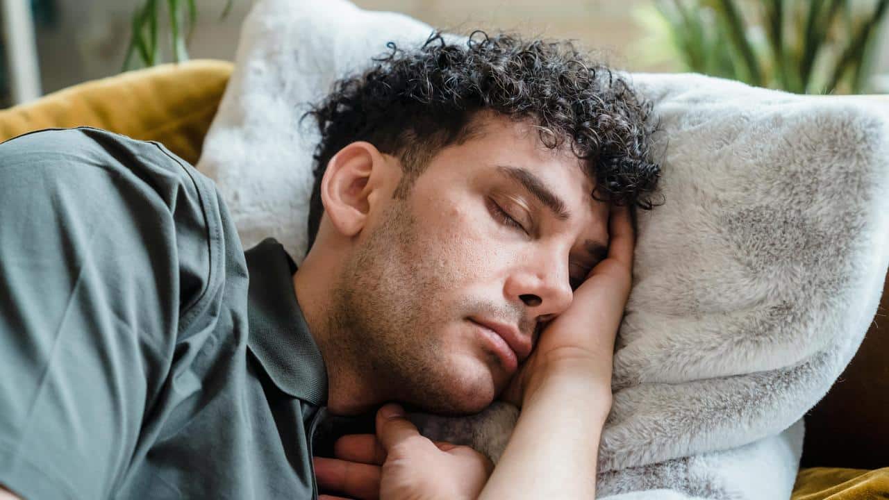 A man sleeping on a soft pillow with his hand against his face.