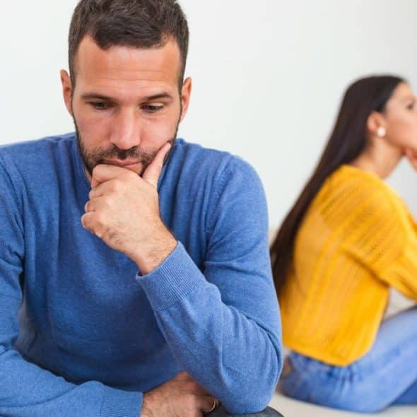 A man in blue is looking down, while a woman in yellow sits behind him.