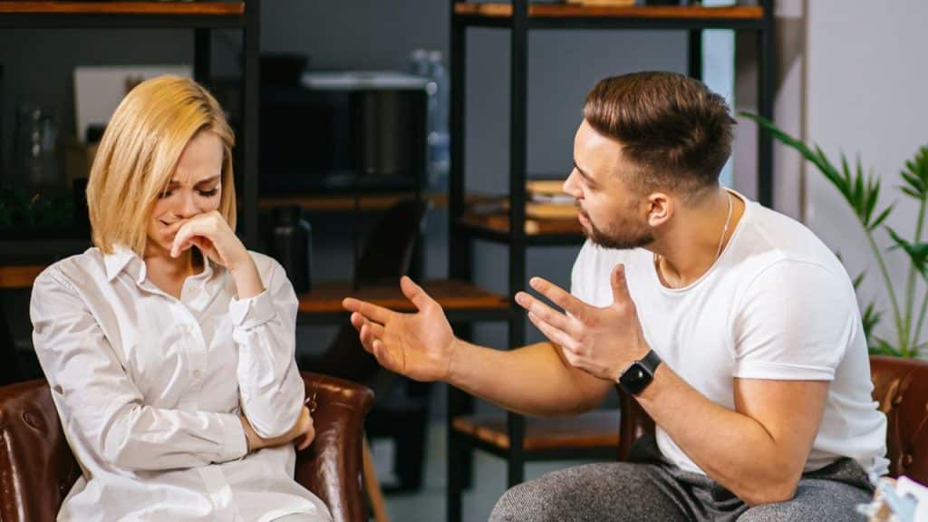 A man gestures while talking to a crying woman who is covering her mouth.