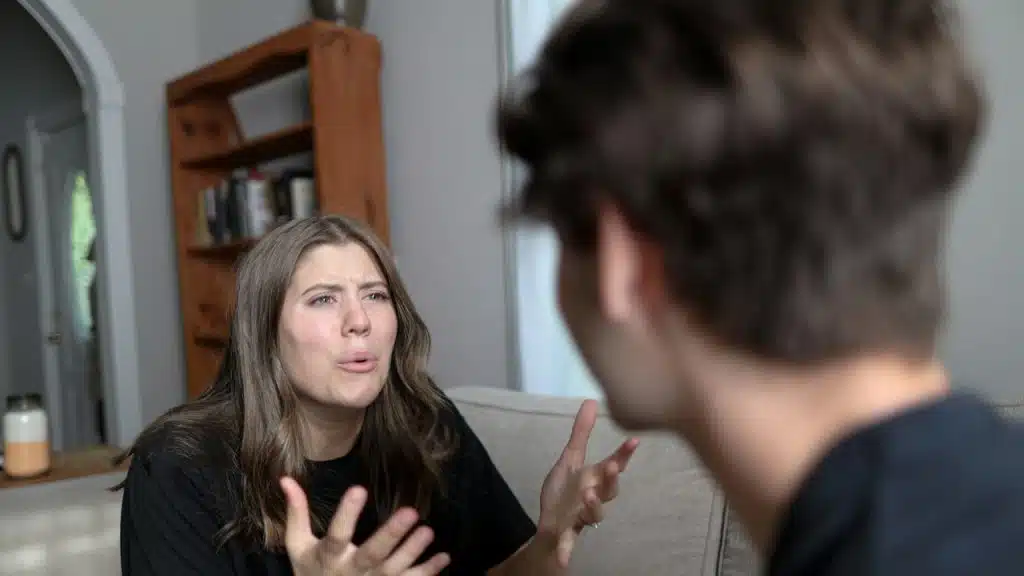 A depressed woman complaining to her husband while sitting on a couch talking to her husband.