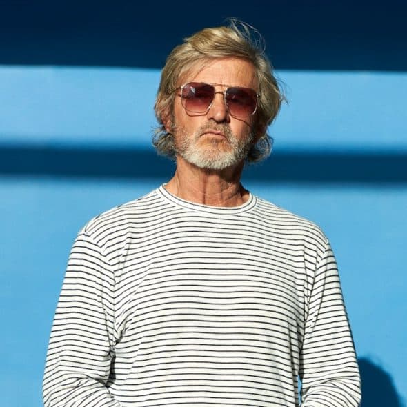 A middle-aged man standing in front of a blue wall.