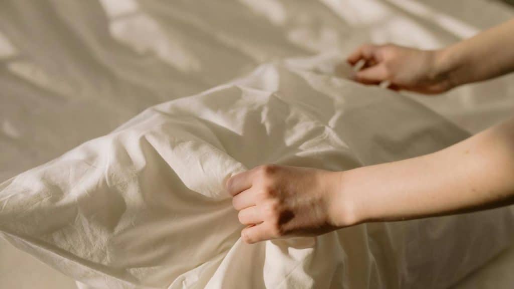 A person adjusting a pillow on a neatly made bed.