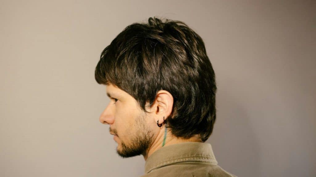 Side profile of a man with dark hair, a beard, and black earrings.