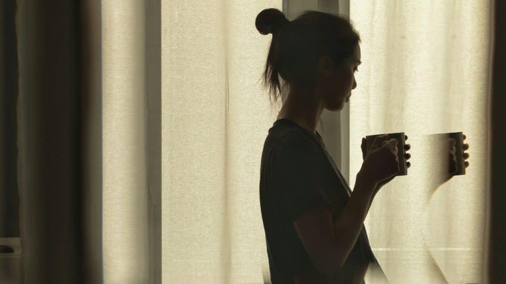 Silhouette of a woman holding a cup, standing near sheer curtains.