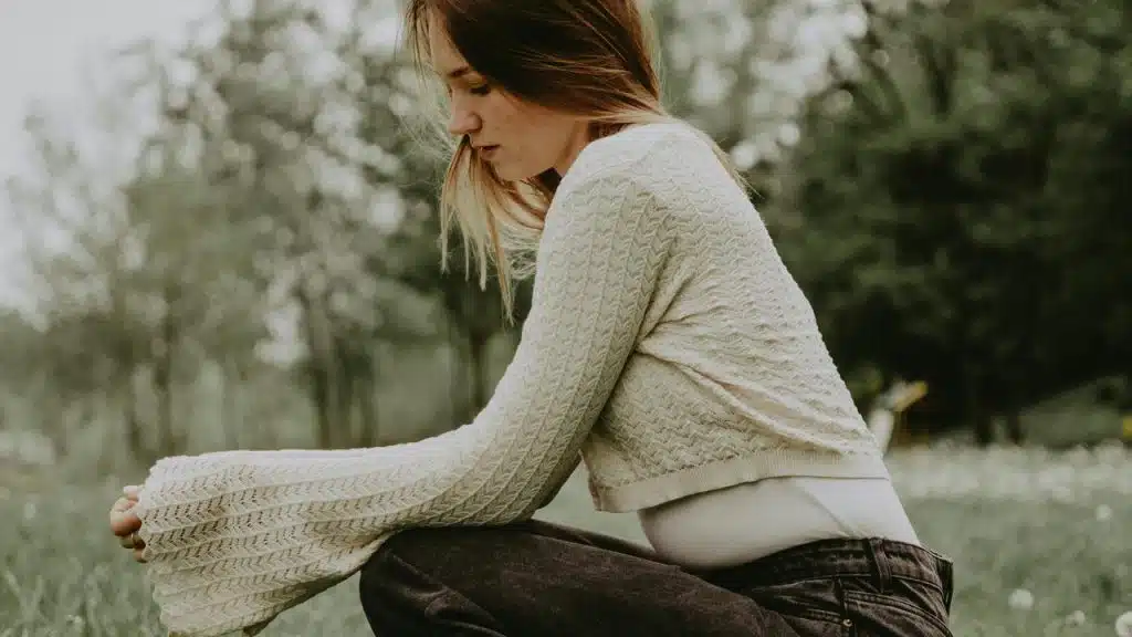A woman sitting outdoors in a park looking down thoughtfully.