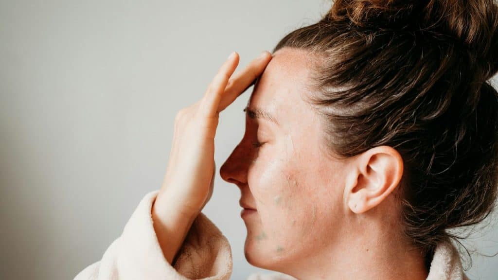 Profile view of a woman with closed eyes and hand touching her forehead indoors.