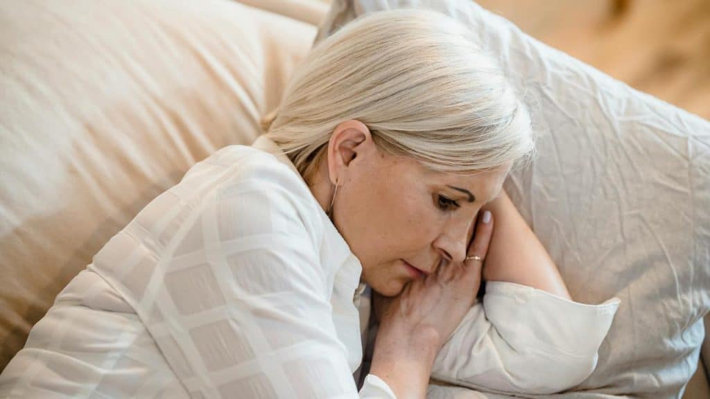 A woman lying in bed resting her head on a pillow.