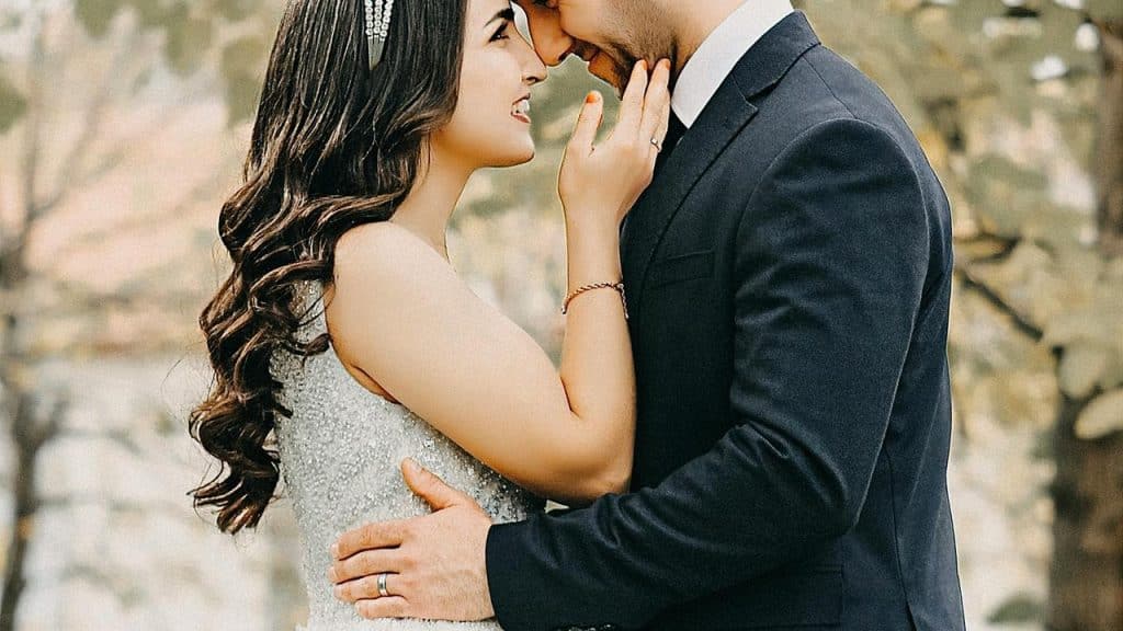 A bride and groom embrace closely, smiling with their foreheads touching.