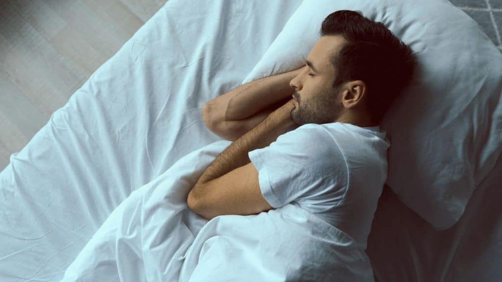 Overhead view of a man sleeping peacefully on a bed with white sheets and a pillow.