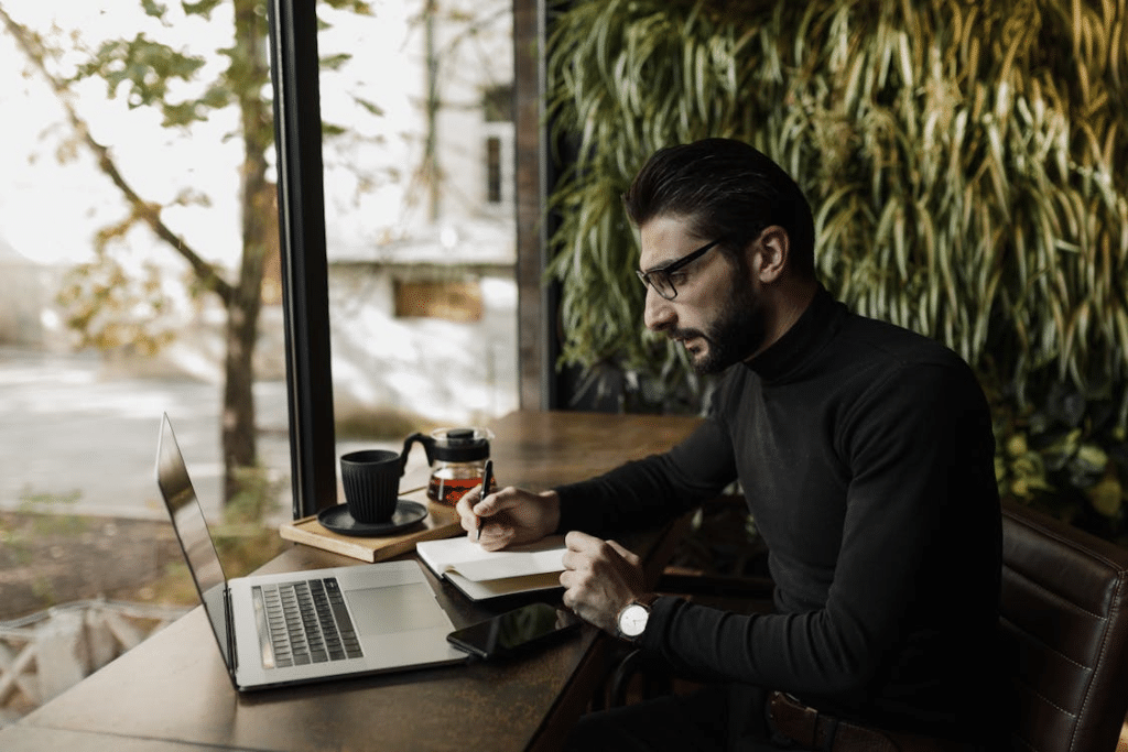 A man writing on a table with a laptop