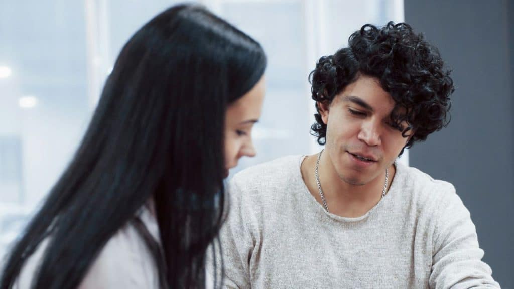 A curly-haired man in a light sweater sits close to a woman with long dark hair.