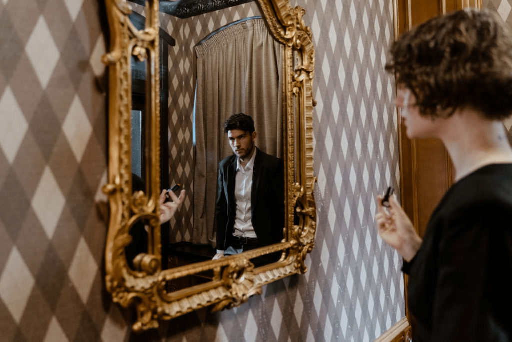 A Mirror Reflection of a Man in Black Suit Jacket Standing Near a Woman Facing a Mirror