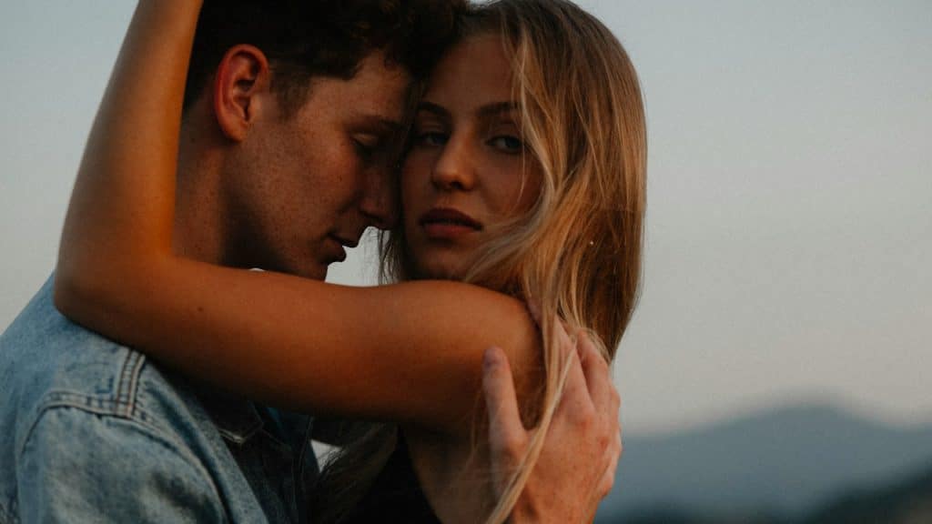 Side view of a young couple hugging in countryside at sunset.