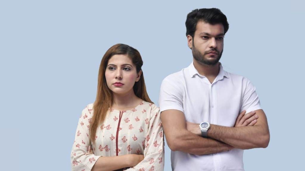 A serious man and woman stand side-by-side with crossed arms against a blue background.