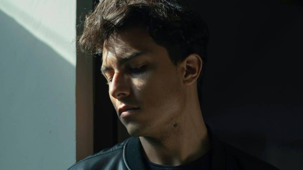 Young man with dark, messy hair looking down in deep shadow and harsh sunlight.