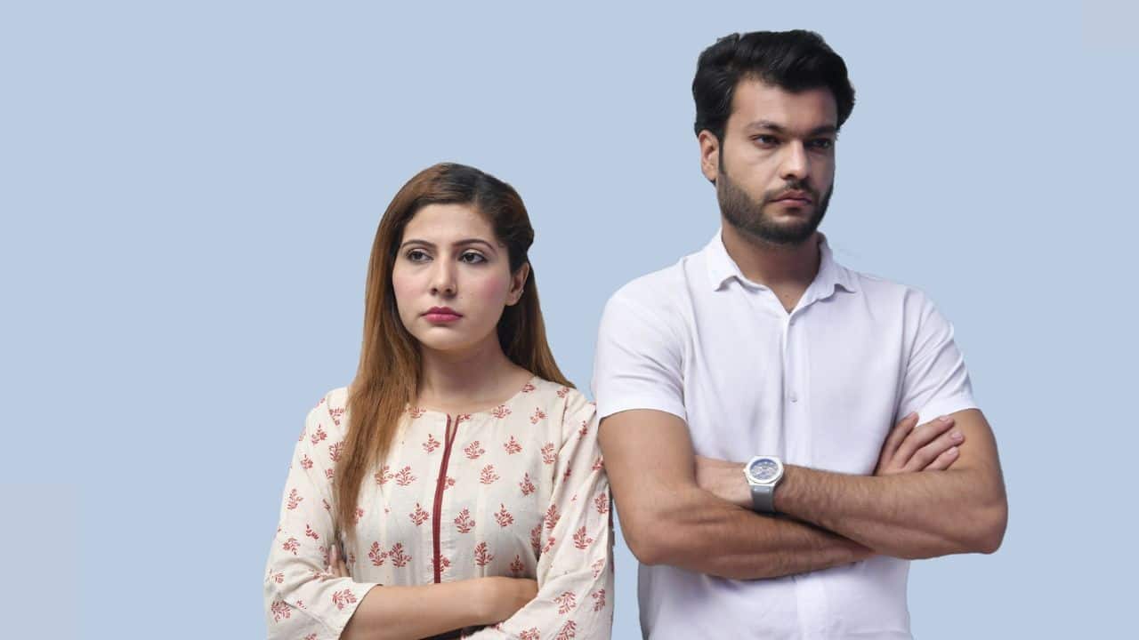 A serious man and woman stand side-by-side with crossed arms against a blue background.