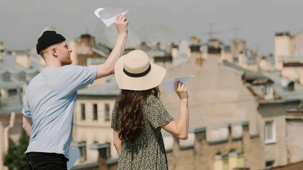 A man and woman holding paper airplanes while standing on a rooftop.