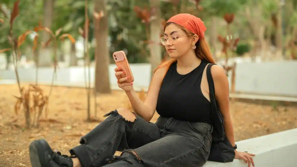 A woman sitting on a boundary wall and looking at his phone.