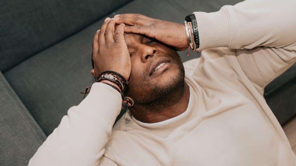 Man lying down with both hands covering his forehead and eyes.
