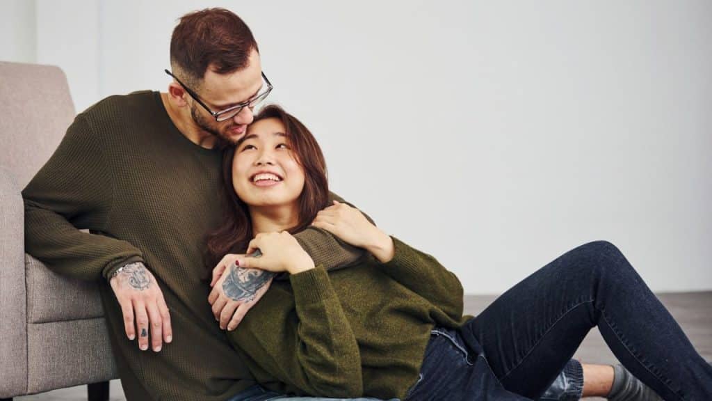 Young couple embracing on the floor, smiling and wearing matching green sweaters.