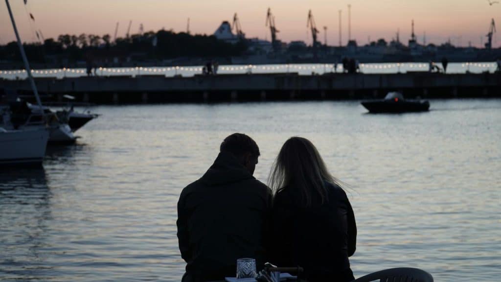 A couple sits by the water at sunset, quietly enjoying the view together.