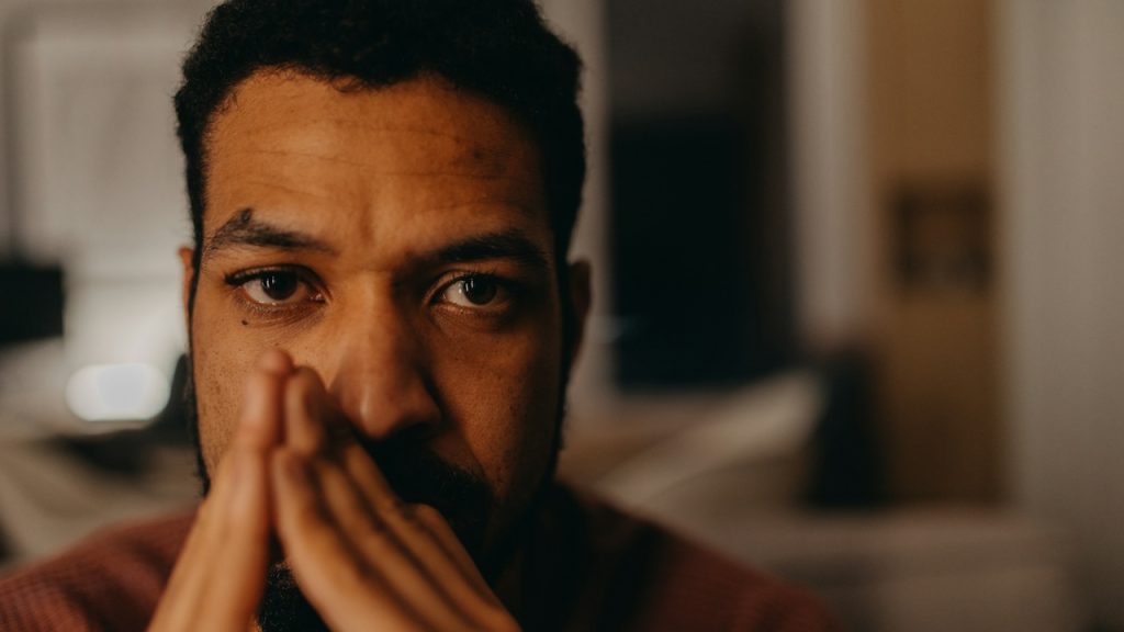 A bearded man looking distraught and holding his hands up to his face.
