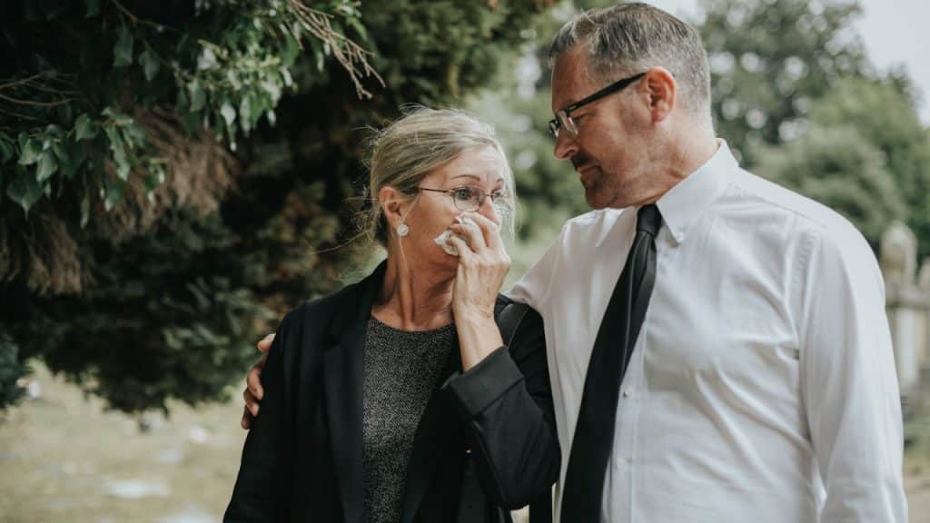 Man comforting a crying woman wiping her face with a tissue outdoors.
