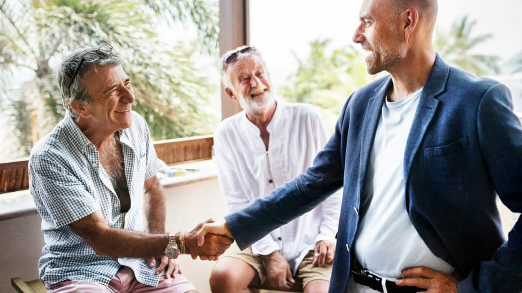 A group of older men smiling as two of them shake hands.