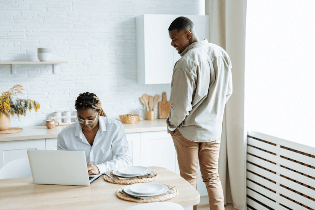 A Woman Using a Laptop at the Table While a Man Standing Beside Her