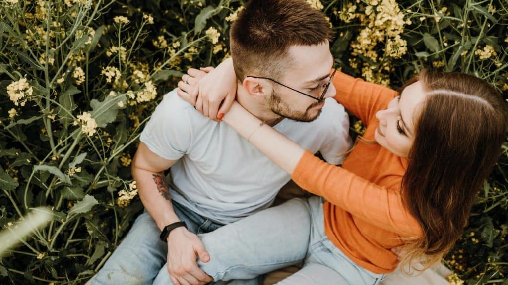 A couple sitting closely together in a field of yellow flowers, gazing into each other’s eyes.