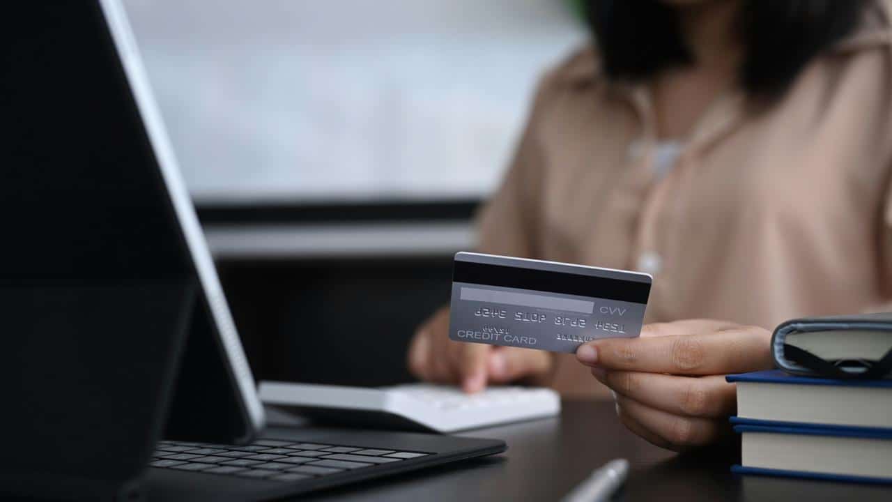 A woman holding a credit card while using a laptop.