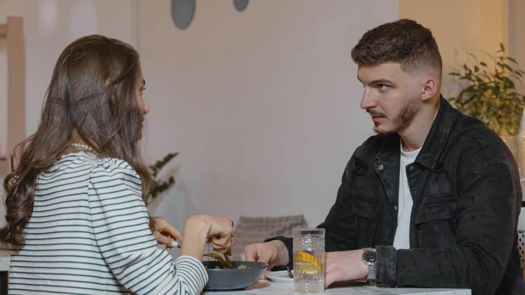 A man and woman sitting at a table having a serious conversation over a meal.
