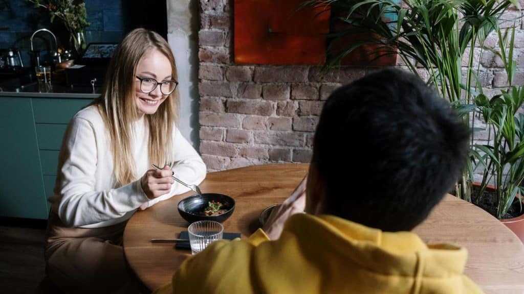 A woman smiling at someone across the table while eating in a cozy cafe.