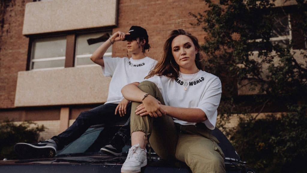 A couple sitting on the hood of a car.