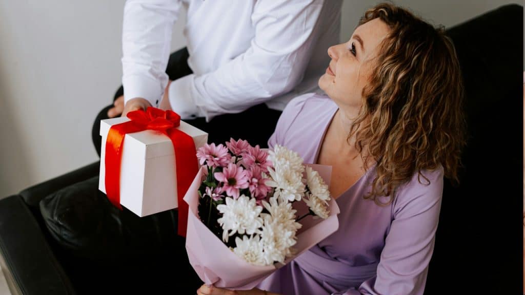 A man giving a present and a bouquet of flowers to his wife.