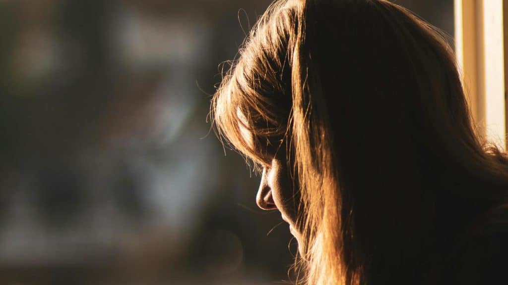 A woman in soft sunlight looking downward in a quiet, reflective moment.