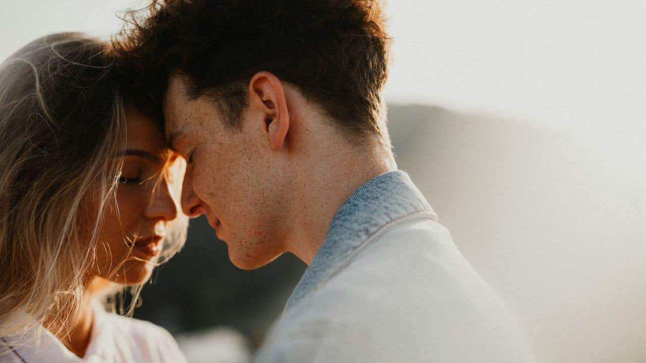 A man and a woman with their foreheads touching are embracing in warm, natural light.