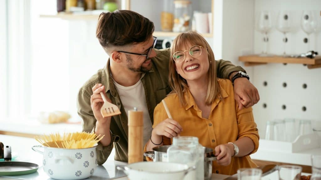 A cheerful couple making pasta at home together.