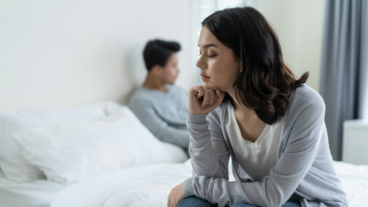 A young couple having conflict is sitting on the bed.