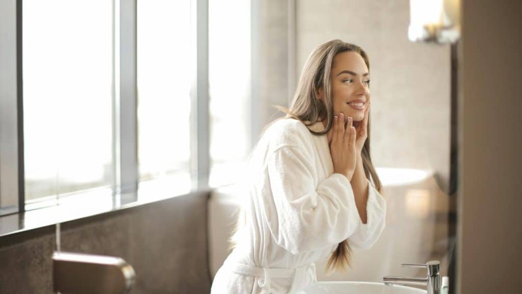 A woman smiling at herself in a bathroom mirror.
