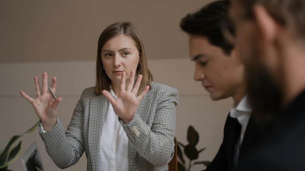 A woman raising her hands while talking to colleagues during a meeting.