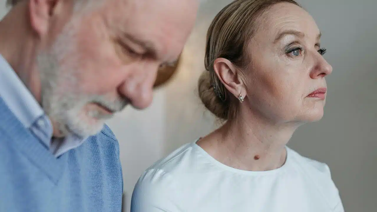 An older couple sitting together, both looking downcast.