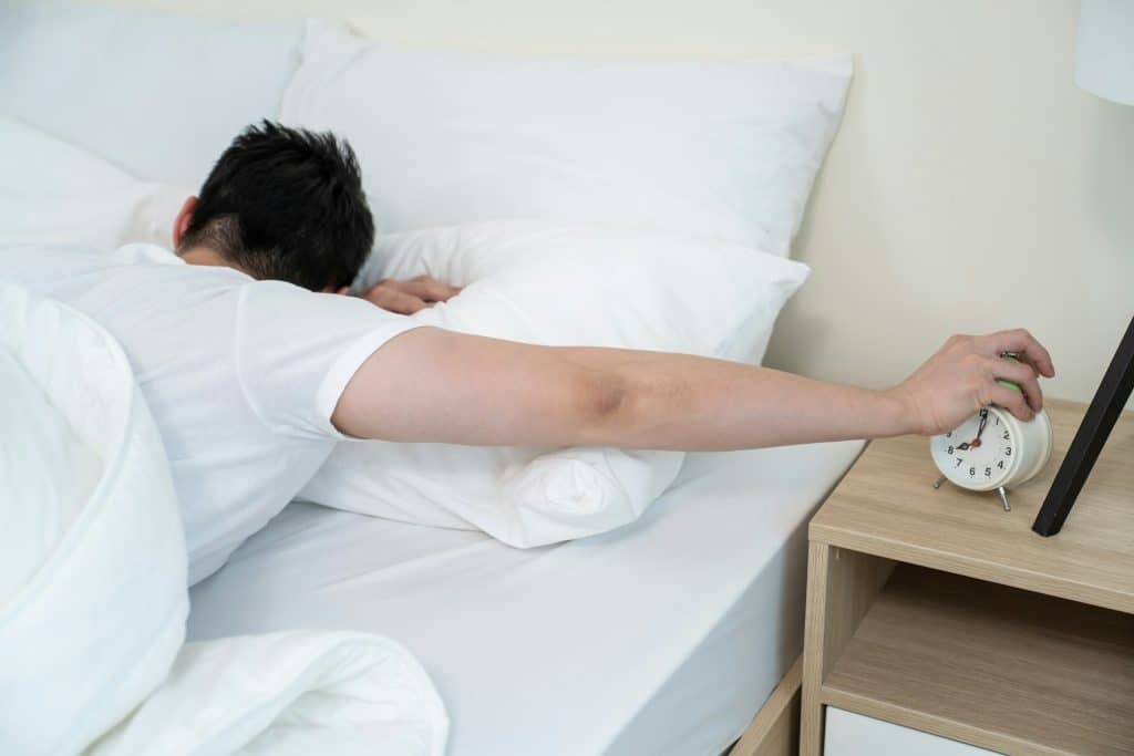 A man turning off an alarm clock.