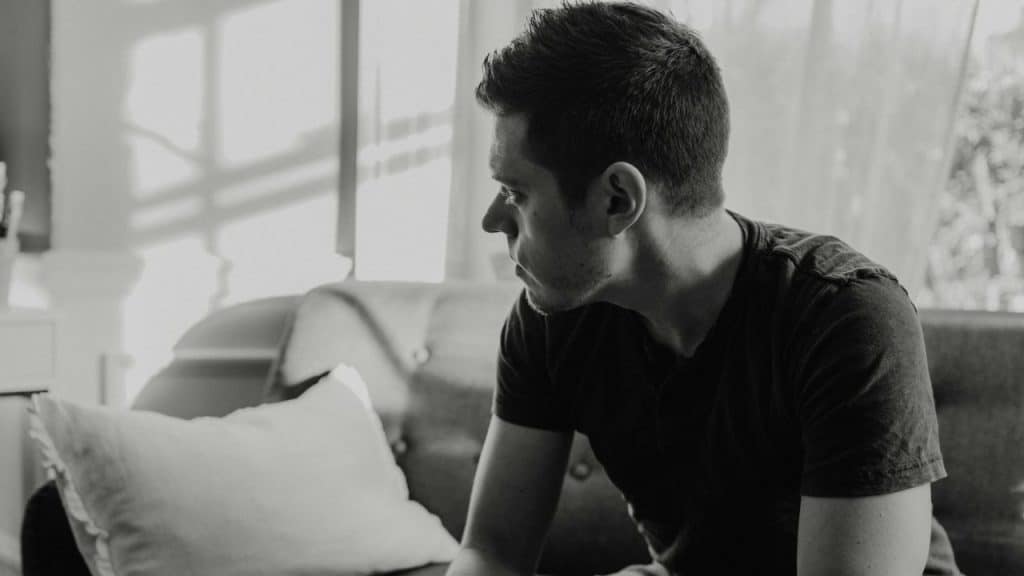 Black and white image of a man sitting on a sofa looking away thoughtfully.