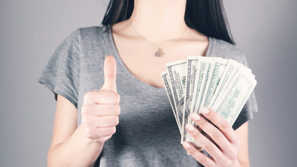 A woman holding money in one hand and giving a thumbs up with the other.