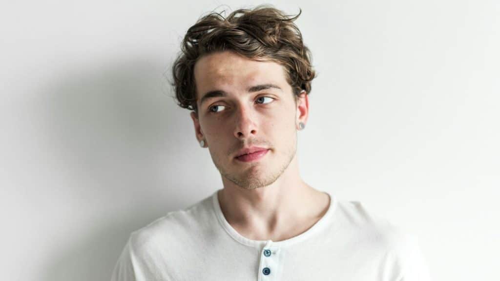 Young man with curly brown hair and a white shirt looking away.